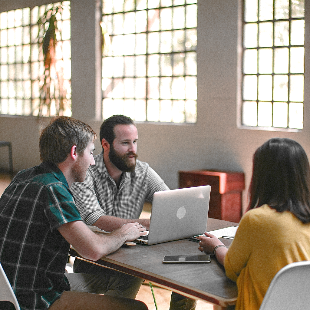 A group of 3 SEO specialists discusses client strategy at their desks in a bright, modern office.
